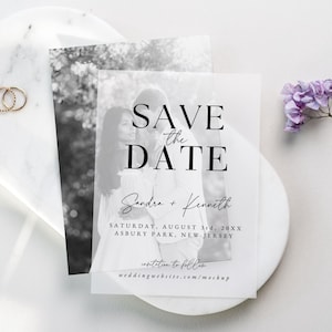 Puede incluir: Una tarjeta de Save the Date con una foto en blanco y negro de una pareja, superpuesta con texto. El texto dice "SAVE the DATE" e incluye los nombres "Sandra + Kenneth" y los detalles del evento. La tarjeta está sobre una superficie blanca con detalles florales.