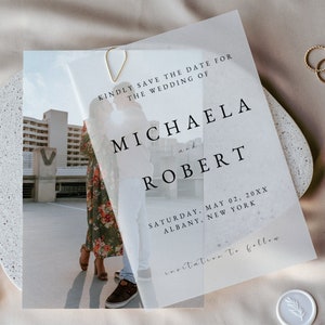 May include: A save the date card with a photograph of a couple in the background. The text reads "Kindly save the date for the wedding of Michaela and Robert, Saturday, May 02, 20XX, Albany, New York. Invitation to follow."