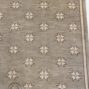 May include: A beige rug with a repeating pattern of white starbursts. The rug has a subtle texture and a simple design.