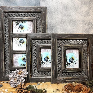 May include: Three ornate wooden picture frames with a dark brown finish. The frames have intricate carvings and are arranged in a descending size order. Each frame features a photo of a blue flower.
