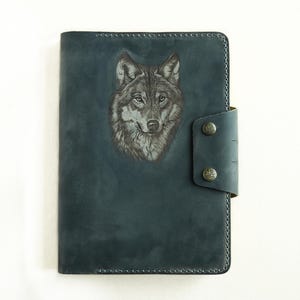 May include: A dark blue leather journal with a wolf head design embossed on the front cover. The journal has a flap closure with two brass snaps.