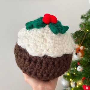 May include: A crocheted Christmas pudding ornament with a white top and brown bottom. The ornament is decorated with green holly and red berries.