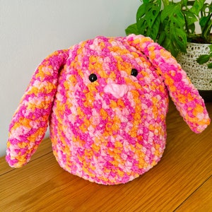 May include: A pink and orange crocheted bunny toy with black eyes and a pink nose.