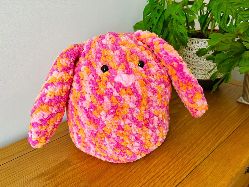 May include: A pink and orange crocheted bunny toy with black eyes and a pink nose.