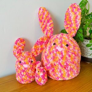May include: Three crocheted bunnies in pink and orange. The largest bunny is sitting upright with its ears up. The middle bunny is sitting with its ears down. The smallest bunny is sitting with its ears down.