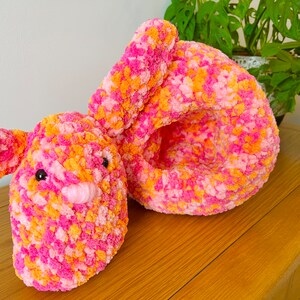 May include: A pink and orange crocheted bunny toy with black eyes and a pink nose. The bunny is lying on its side with its head resting on its arm.