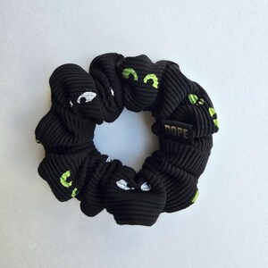 May include: Black scrunchie with a white and green eye pattern and the word "DOPE" in gold lettering.
