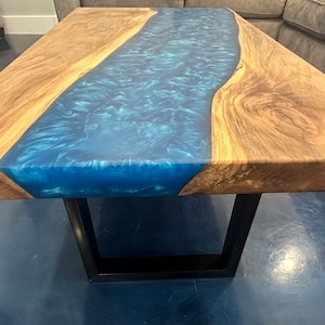 May include: A wooden coffee table with a blue resin river running through the center. The table has a black metal base.