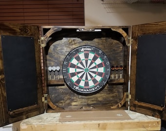 Puede incluir: Un armario de madera para dardos con dos puertas que se abren para revelar un tablero de dardos, soportes para dardos y una pizarra. El tablero de dardos es un tablero de dardos "Accu-Sport Tournament" negro y verde.