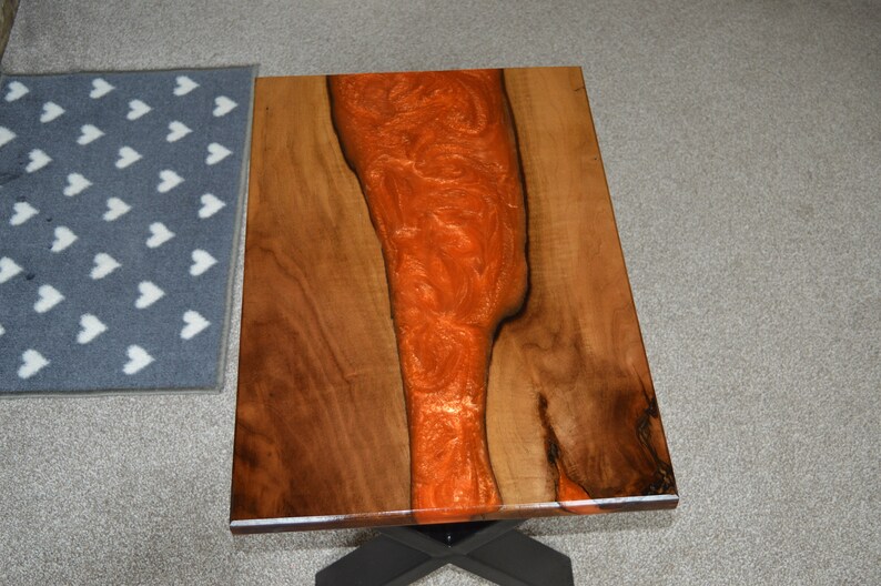 May include: A wooden coffee table with a live edge top and a black metal base. The top is finished with a clear epoxy resin with a copper-colored swirl.