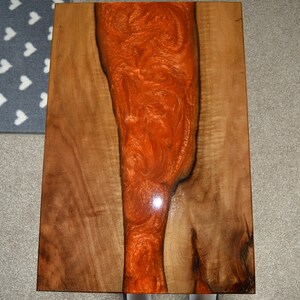 May include: A wooden table top with a large orange resin inlay. The resin has a swirling pattern and a glossy finish.