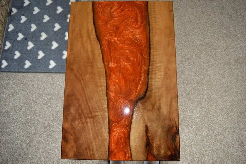 May include: A wooden table top with a large orange resin inlay. The resin has a swirling pattern and a glossy finish.