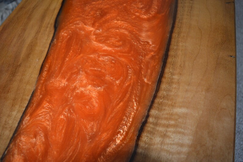 May include: A close-up of a wooden table top with a large orange resin inlay. The resin has a swirling pattern and a glossy finish.