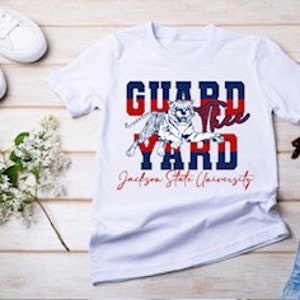 May include: White t-shirt with a red, white, and blue graphic that says "Guard the Yard" with a tiger illustration and the text "Jackson State University".