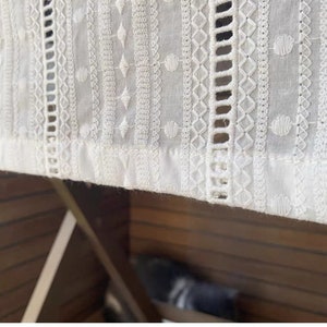 May include: White cotton fabric with intricate embroidered patterns. The fabric has a delicate, lacy look and is perfect for a variety of crafting projects.