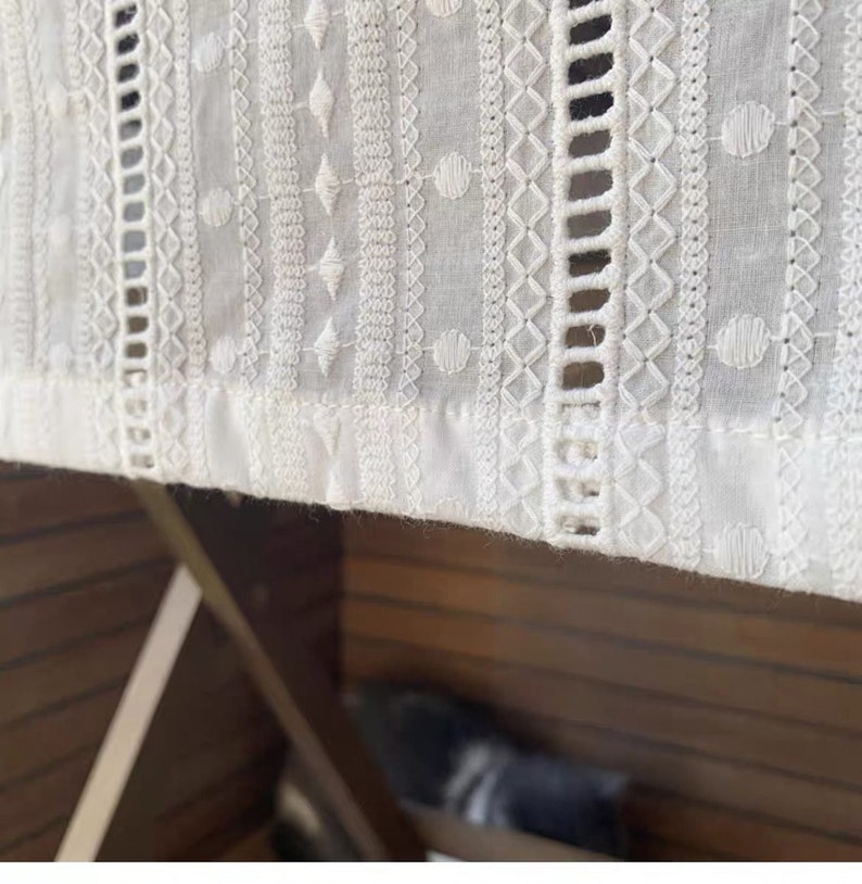 May include: White cotton fabric with intricate embroidered patterns. The fabric has a delicate, lacy look and is perfect for a variety of crafting projects.