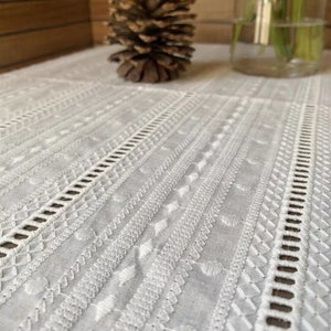 May include: White cotton table runner with an embroidered design featuring a repeating pattern of geometric shapes and lines.