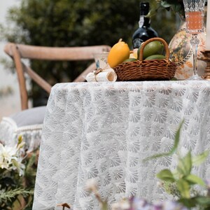 May include: White lace tablecloth with a delicate pattern, set for a summer picnic with a basket of lemons and limes, a glass of wine, and a vintage teacup.