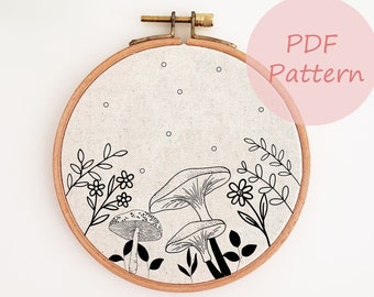 May include: An embroidered hoop art piece with a black and white mushroom and floral design. The design is on a neutral linen fabric, held within a wooden hoop. The text "PDF Pattern" is visible.