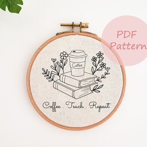May include: A round embroidery hoop with a beige fabric featuring a black line drawing of a coffee cup, books, and floral elements. The text "Coffee. Teach. Repeat" is below the design.