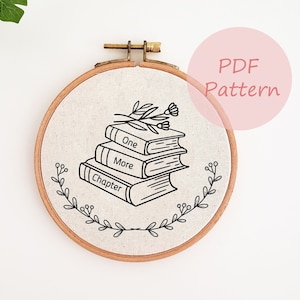 Peut inclure: Broderie sur tissu beige dans un cercle en bois. Le motif noir représente une pile de trois livres avec les mots "One", "More" et "Chapter". Un motif floral et les mots "PDF Pattern" sont également visibles.