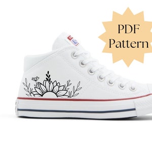 May include: White canvas sneaker with a black floral design featuring a sunflower and leaves. The shoe has white laces, a red and blue stripe on the sole, and the text "PDF Pattern" in a starburst shape.