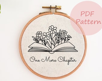 May include: A circular embroidery hoop with a linen fabric displaying a black line drawing of an open book with flowers and the text "One More Chapter." The words "PDF Pattern" are in a pink circle.