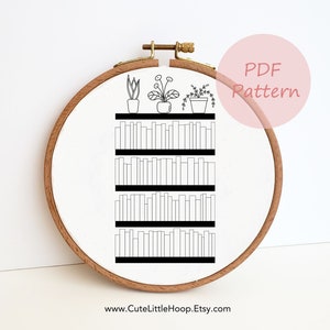 May include: A black and white line drawing of a bookshelf with four shelves filled with books and three potted plants on the top shelf. The image is in a white embroidery hoop with a wooden frame. The text "PDF Pattern" is in a pink circle above the hoop. The text "www.CuteLittleHoop.Etsy.com" is below the hoop.