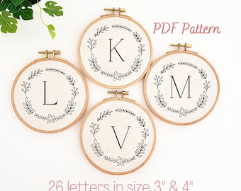 May include: Four embroidery hoops with the letters K, L, M, and V, each surrounded by a floral wreath design. The text "PDF Pattern" and "26 letters in size 3" & 4"" are also visible.