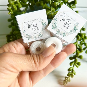 Può includere: Due caramelle alla menta bianche con un design floreale verde e bianco sulla confezione. La confezione dice "Mikey & Jasmine Mint to be 5.25.24".