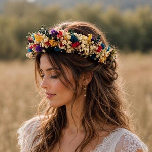 May include: A floral crown featuring a dense arrangement of dried flowers in vibrant shades of red, yellow, blue, and white. The circular headpiece is composed of small, textured blossoms and greenery, creating a colorful and detailed accessory.