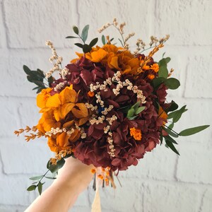 May include: A bouquet of dried flowers in shades of burgundy, orange, and cream. The bouquet includes hydrangeas, baby's breath, and eucalyptus.