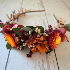 May include: A floral headband with dried flowers in shades of orange, red, and yellow. The headband is made with a wire base and is decorated with small sprigs of dried flowers.