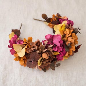 Op de afbeelding: Een witte keramische mok met een zwarte handgreep en de tekst "But First, Coffee" in een vetgedrukte, zwarte letter. De mok is gevuld met een donkere vloeistof, waarschijnlijk koffie, en staat op een wit oppervlak.