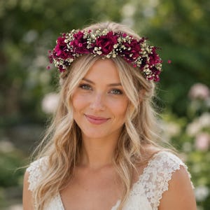 Op de afbeelding: Een bloemenkrans met diep bordeauxrode rozen afgewisseld met kleine witte gipskruidbloemen. Het cirkelvormige hoofddeksel wordt op het voorhoofd gedragen en toont een dicht arrangement van donkerrode bloesems en fijne witte opvulbloemen.
