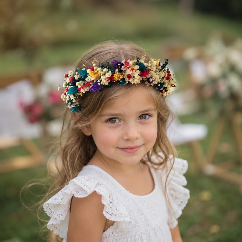 May include: A floral crown featuring a vibrant arrangement of dried flowers in shades of red, yellow, purple, and teal, accented with cream-colored baby's breath. The circular headpiece is constructed from small, delicate blossoms and foliage.