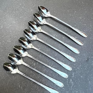 May include: A set of eight silver teaspoons with a decorative design on the handle. The spoons are arranged in a row, with the handles pointing to the right.