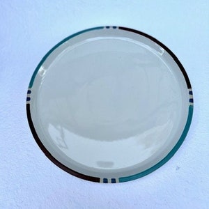 May include: A white ceramic plate with a brown and blue rim. The rim has a geometric pattern.