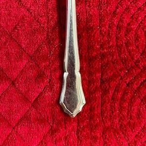 May include: A silver-colored fork with a decorative handle. The handle has a scalloped design and a pointed tip.