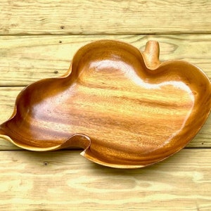 May include: A large, wooden serving bowl shaped like a leaf. The bowl is made of a light brown wood and has a smooth, polished finish.