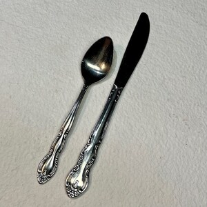 May include: A silver spoon and butter knife with ornate handles. The spoon has a rounded bowl and the knife has a pointed tip.