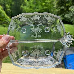 May include: A clear glass divided serving dish with an etched design of palm trees. The dish has a scalloped edge and two handles.