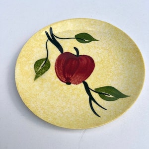 May include: A yellow ceramic plate with a red apple and green leaves painted on it.