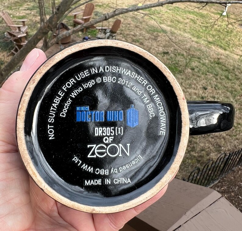 May include: Black ceramic mug with a handle, featuring the Doctor Who logo and text. The bottom of the mug has the text "NOT SUITABLE FOR USE IN A DISHWASHER OR MICROWAVE". The mug is marked "MADE IN CHINA".