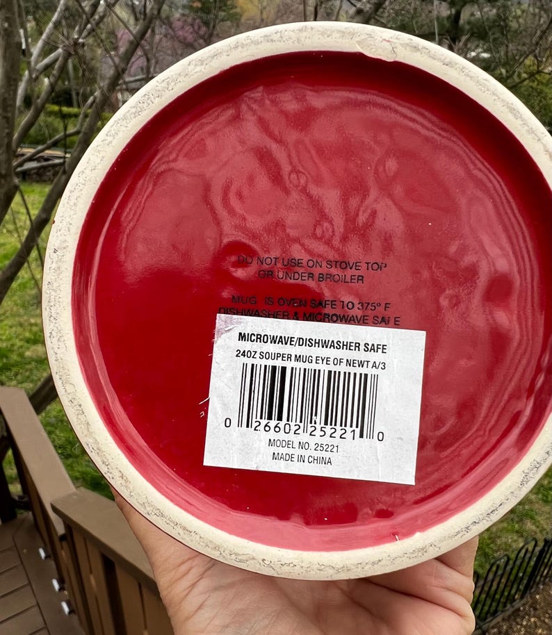May include: A red ceramic mug with a white rim. The bottom of the mug has a label that reads "MICROWAVE/DISHWASHER SAFE" and "240Z SOUPER MUG EYE OF NEWT A/3". The mug is oven safe to 375&deg;F.