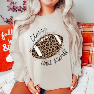 May include: A beige sweatshirt with a leopard print football design and the text "Classy Until Kickoff".