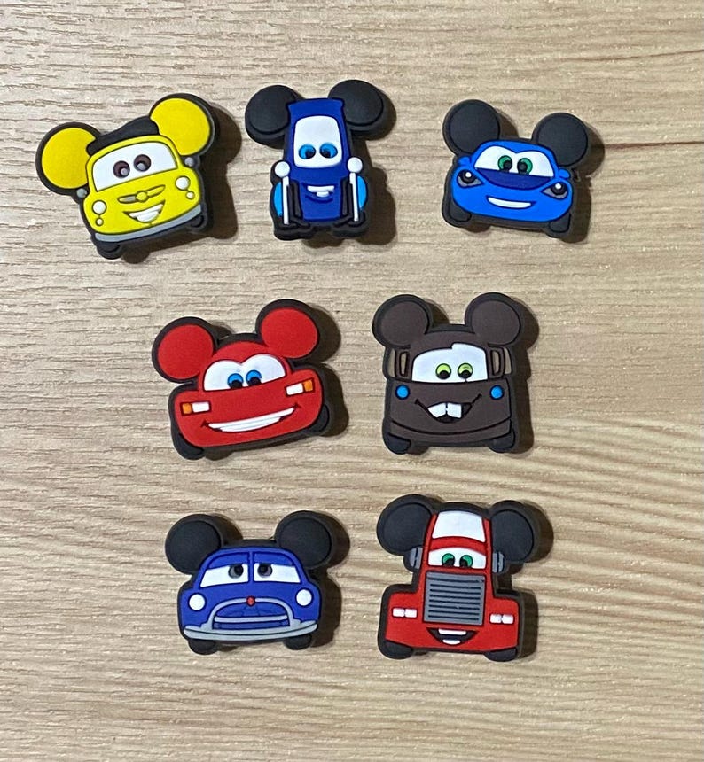 May include: Set of seven colorful cartoon car shoe charms with Mickey Mouse ears. The cars are red, blue, yellow, and brown.