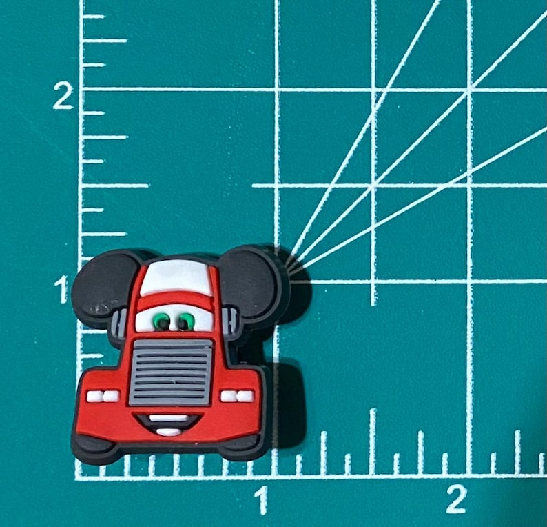 May include: Red cartoon truck with black Mickey Mouse ears. The truck has a white windshield and a gray grill. The truck has a smiling face with green eyes.
