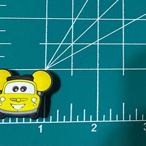 May include: Yellow cartoon car with black eyes and a smiling mouth. The car has large, round ears on the sides.