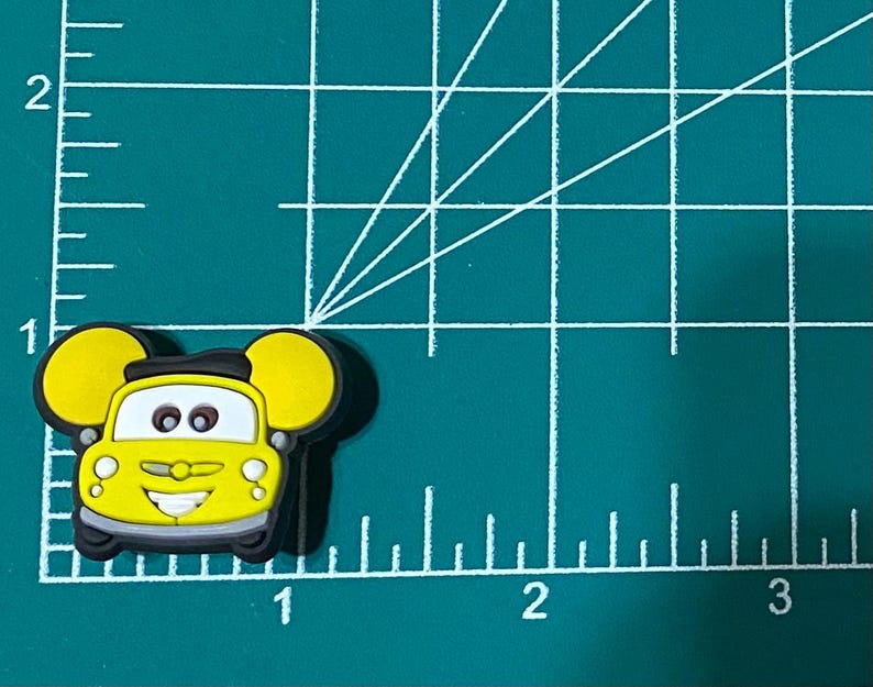 May include: Yellow cartoon car with black eyes and a smiling mouth. The car has large, round ears on the sides.